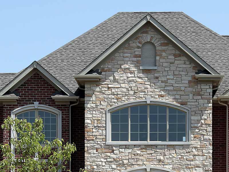 Close-up of a residential home with rocky siding and a gray asphalt shingle roof